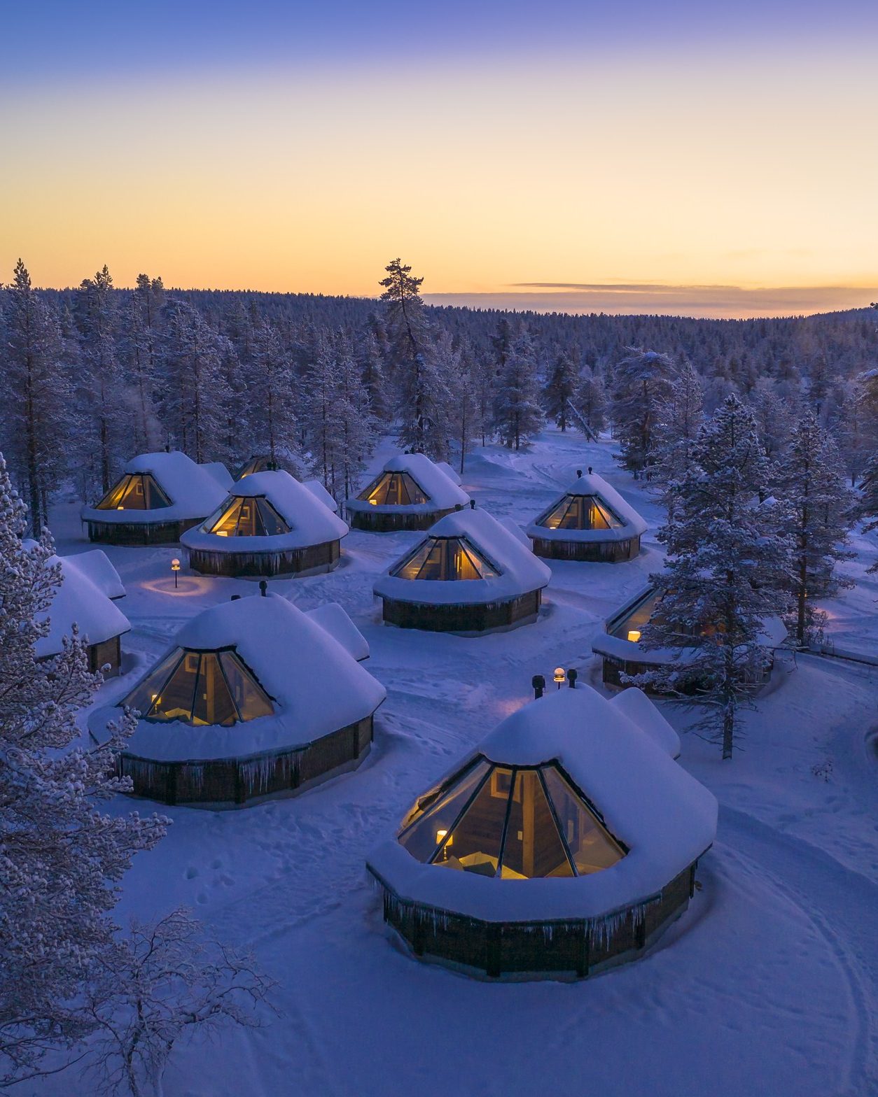 Aurora Cabins mit beheiztem Glasdach im verschneiten Wald in der Dämmerung